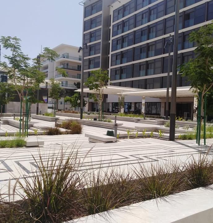 Patterned paving with ornamental grasses and young trees beside a mixed-use building